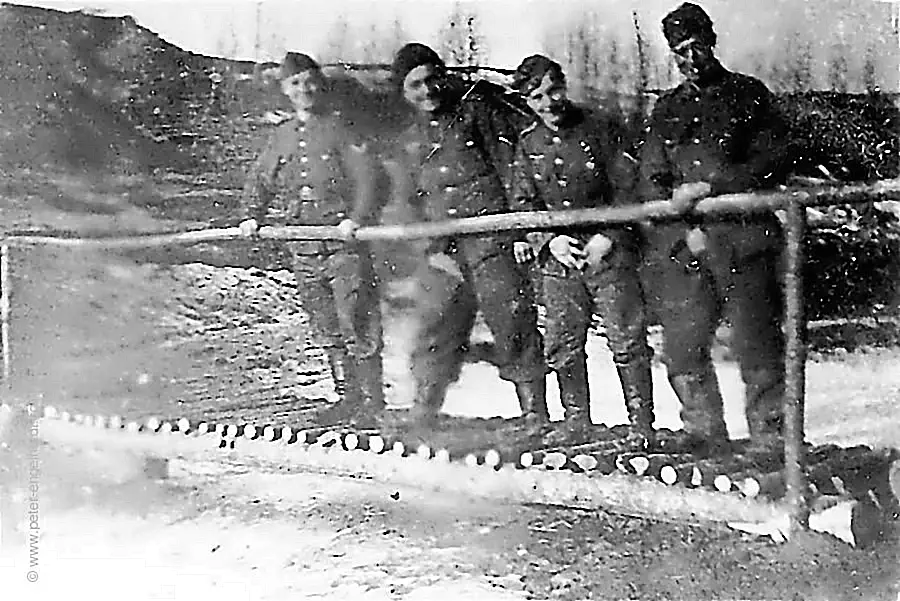Vier angetrunkene Soldaten pinkeln im Stützpunkt "Remscheid" bei Kholm 1943 von einem hölzernen Steg in den Schnee.