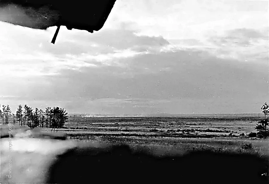 View from a camouflaged artillery observation post across a vast plain where distant shell impacts can be seen.