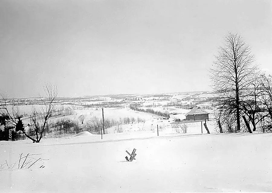 Blick auf eine leicht hügelige schneebedeckte Landschaft im Baltikum mit dem Regimentsgefechtstand im Februar 1944.
